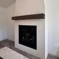 A modern white concrete fireplace mantel with a black firebox insert and a dark wood vertical support beam, shown in an interior setting.